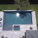 A pool with an outdoor shower and patio furniture.