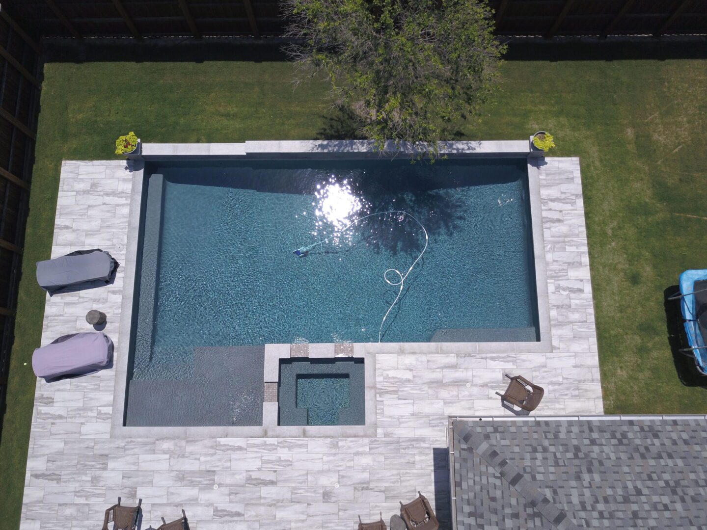 A pool with an outdoor shower and patio furniture.