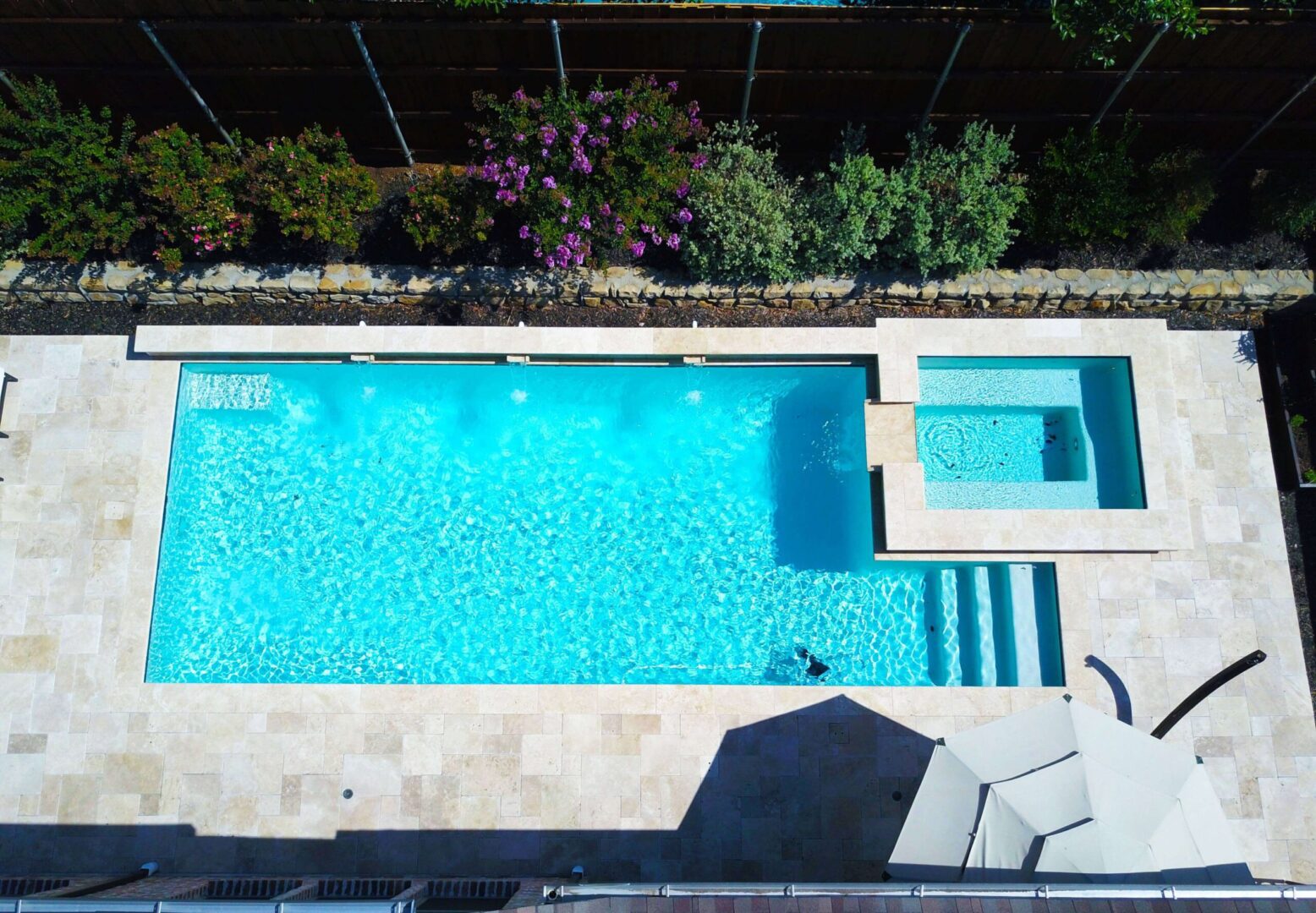 A pool with steps and a hot tub in it.